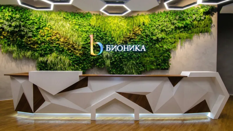 Длинная стойка ресепшн РИ-199 в современном офисном интерьере с зеленой фитостеной.